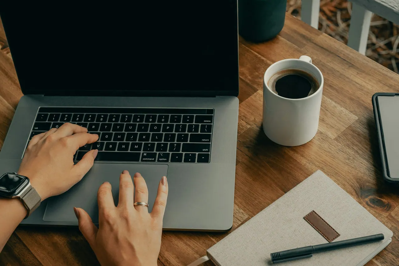 حاسوب محمول على طاولة خشبية بجانب نافذة