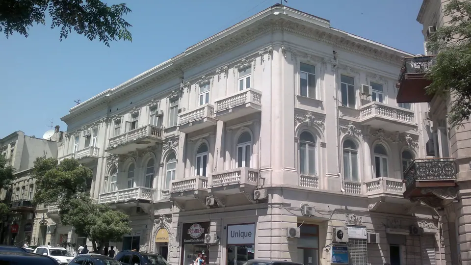 The upper floors of a pale stone building with balconies and arched windows.