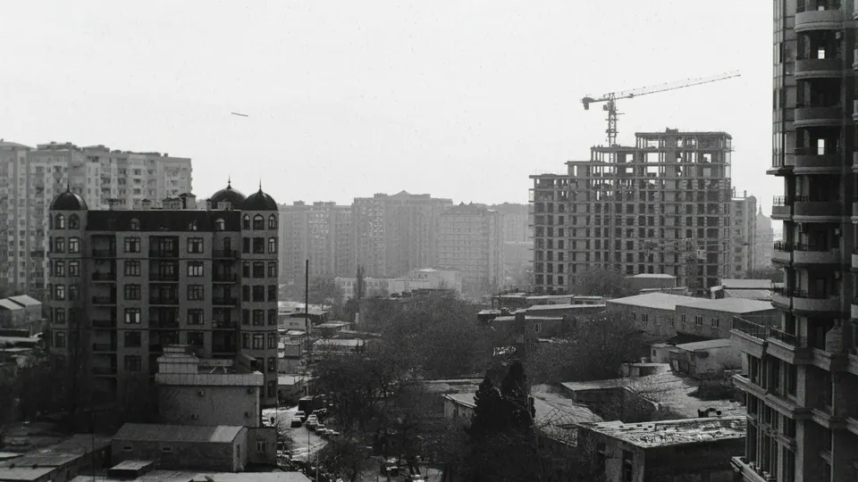 Black-and-white view over Baku apartment buildings, with a building under construction and a crane.