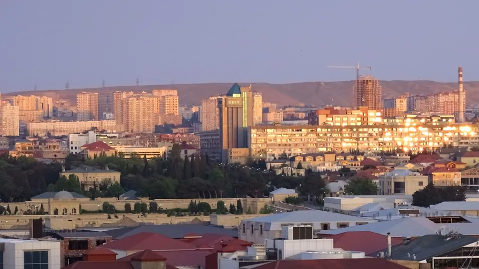 Multi-storey apartment blocks and low-rise houses in Baku in early morning light, with hills behind.