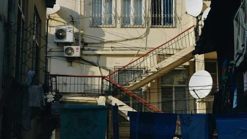 An inner courtyard with an external staircase, barred windows, air-conditioning units, satellite dishes and laundry lines.