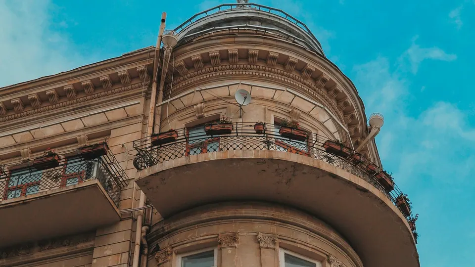 A rounded stone corner of an old apartment building with wrought-iron balconies and flower boxes.