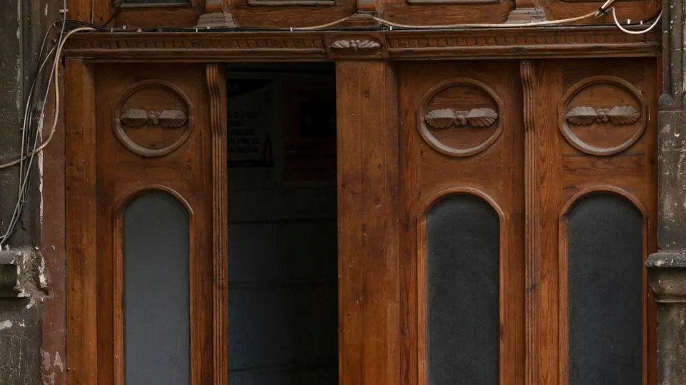 Carved wooden double doors with glass panels, one leaf open onto a dim stairwell.