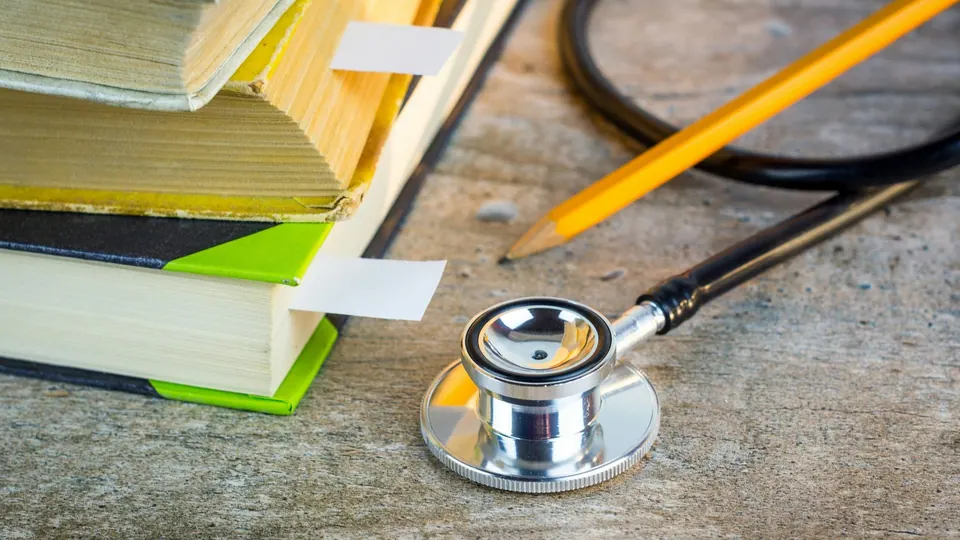 سمّاعة طبية وقلم رصاص أصفر بجانب كومة من الكتب الدراسية المعلَّمة على طاولة خشبية