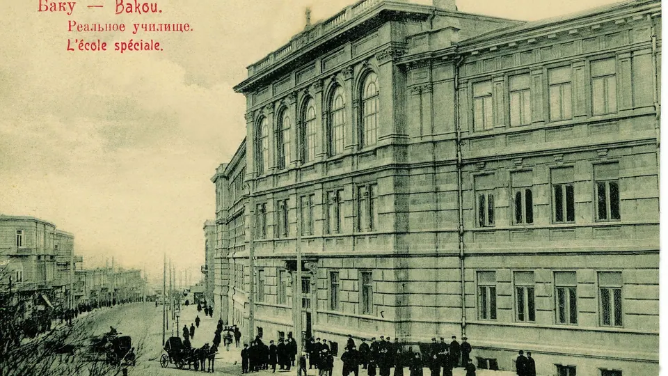 A sepia postcard of a large stone school building on a street with pedestrians and horse-drawn carriages.