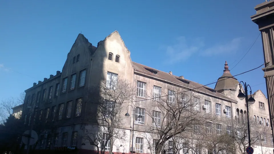 A multi-storey historic building with stepped gables against a blue sky, behind bare trees.