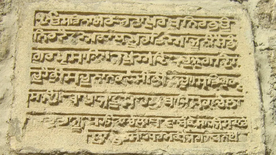 لوح حجري منقوش بعدة أسطر من الكتابة البارزة، مثبّت في جدار من الحجر الرملي.