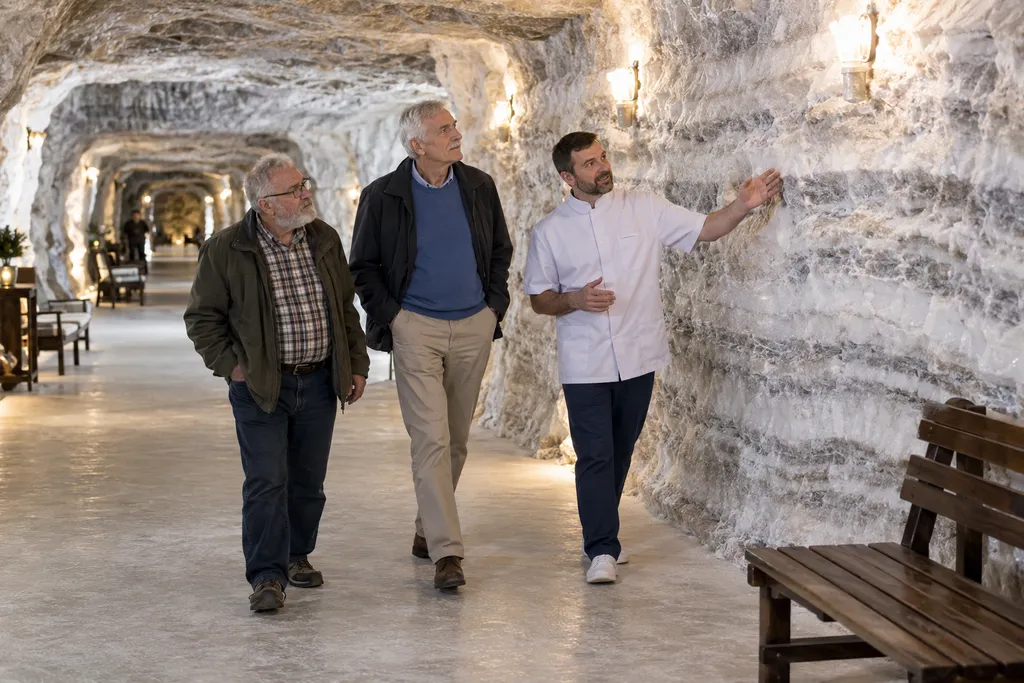 Illustrative image: a guide walking two older visitors through a salt-cave passage