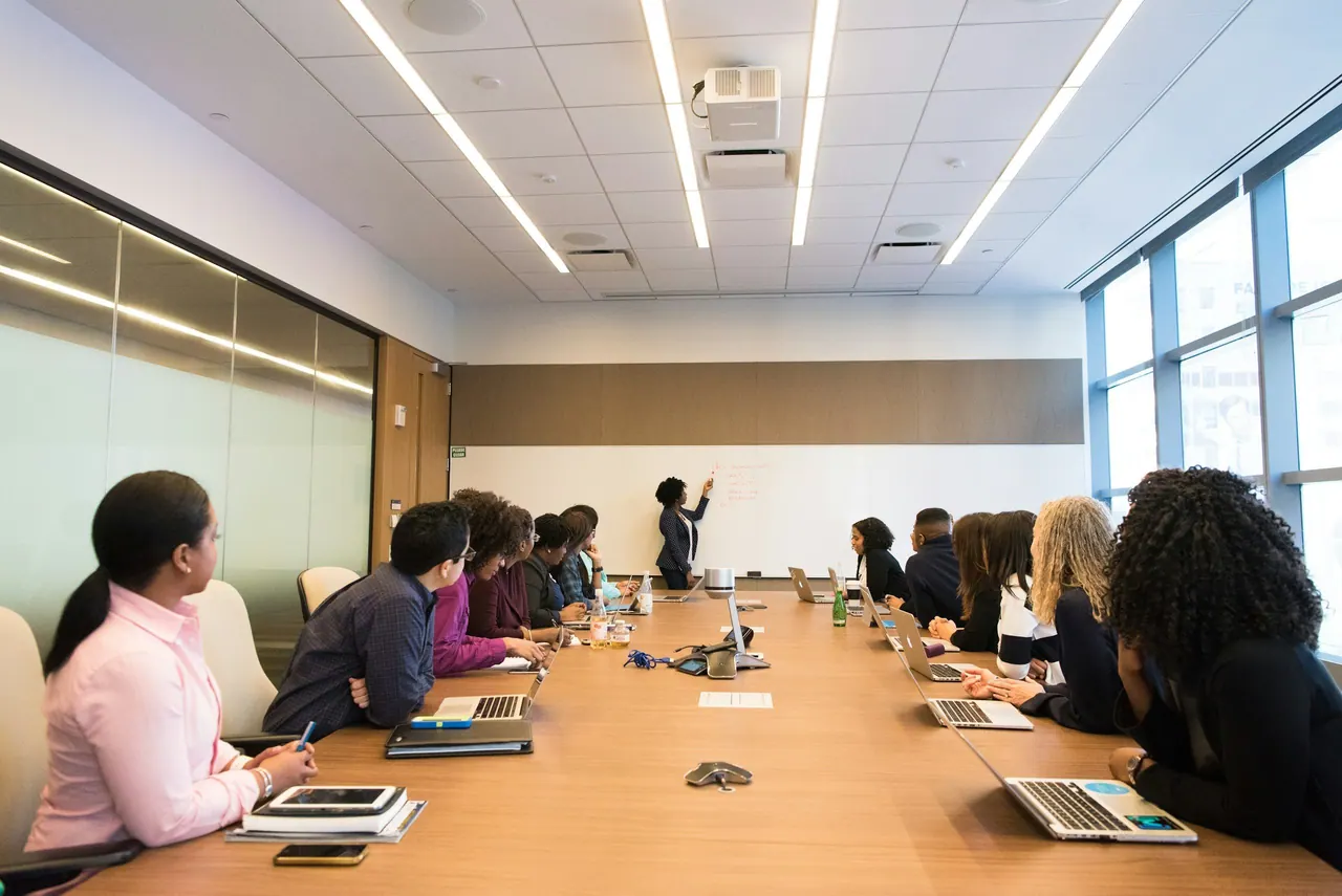 مشاركون حول طاولة اجتماعات طويلة يستمعون إلى متحدث